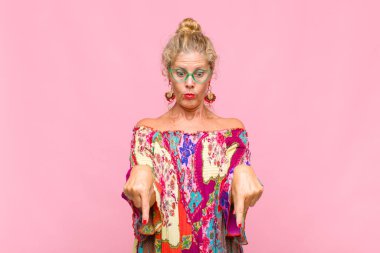 Orta yaşlı, ağzı açık bir kadın iki eliyle aşağıya doğru bakıyor, şaşkın, şaşkın ve şaşırmış görünüyor.