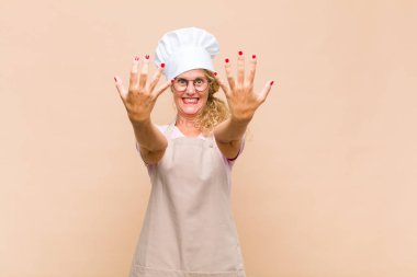 Orta yaşlı kadın fırıncı gülümsüyor ve arkadaş canlısı görünüyor, onuncu veya onuncu numarayı gösteriyor, eli önde, geriye doğru sayıyor.