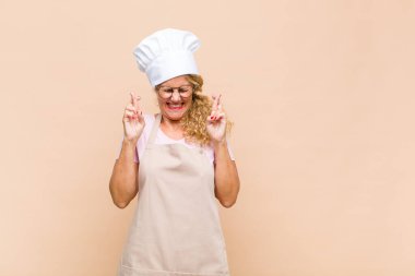 Orta yaşlı fırıncı kadın gülümseyerek ve endişeyle iki parmağını çaprazlayarak endişeli ve iyi şanslar diliyor.