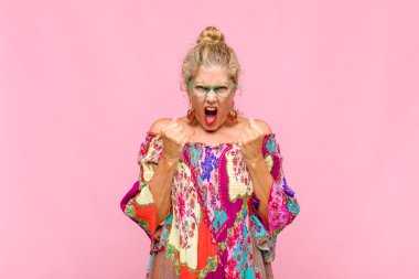 Orta yaşlı bir kadın sinirli, sinirli, kızgın bakışlar ve sıkı yumruklarla bağırıyor. Öfkeli hissediyor.