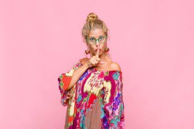 Orta yaşlı bir kadın sessizlik ve sessizlik istiyor, parmağıyla ağzının önünde işaret ediyor, 