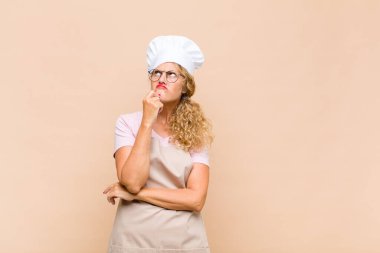 Orta yaşlı fırıncı kadın düşünüyor, kuşkulu ve şaşkın hissediyor, farklı seçeneklerle, hangi kararı vereceğini merak ediyor.