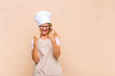 Orta yaşlı kadın fırıncı zaferle bağırıyor, gülüyor, mutlu ve heyecanlı hissediyor başarıyı kutlarken.