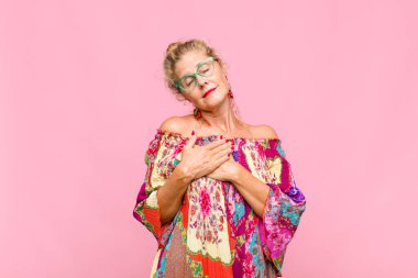 Orta yaşlı bir kadın romantik, mutlu ve aşık, neşeli bir şekilde gülümseyen ve kalbe yakın el ele tutuşan