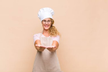 Orta yaşlı fırıncı mutlu bir gülümseme ile güler yüzlü, kendine güvenen, olumlu bakışlı, bir nesne ya da konsept sunan ve gösteren