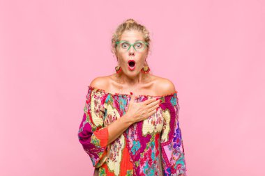 Orta yaşlı bir kadın şaşkın ve şaşırmış hissediyor, gülümsüyor, el ele tutuşuyor, o olmaktan mutlu ya da minnettarlık gösteriyor.