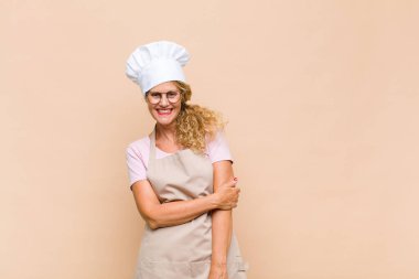 Orta yaşlı fırıncı utangaç ve neşeli bir şekilde gülüyor, arkadaş canlısı, olumlu ama güvensiz bir tavırla.