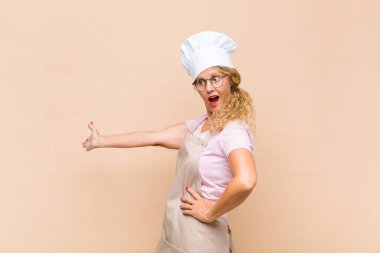 Orta yaşlı bir fırıncı kendini mutlu ve neşeli hissediyor, gülümsüyor ve sizi hoş karşılıyor, dostça bir jestle içeri davet ediyor.