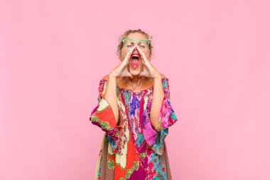 Orta yaşlı kadın mutlu, heyecanlı ve pozitif hissediyor. Elleri ağızda, bağırarak bağırıyor.