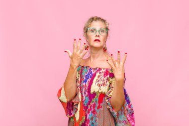 Orta yaşlı bir kadın gülümsüyor ve arkadaş canlısı görünüyor. 9 ya da 9 numarayı gösteriyor. Eli önde, geriye doğru sayıyor.