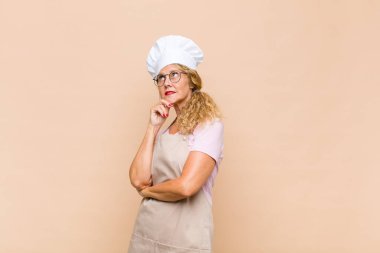 Orta yaşlı fırıncı kadın mutlu bir şekilde gülümsüyor ve hayal kuruyor ya da şüphe ediyor.