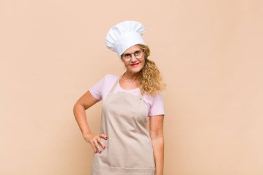 Orta yaşlı fırıncı mutlu bir şekilde gülümsüyor, eli kalçasında ve kendinden emin, olumlu, gururlu ve arkadaş canlısı bir tavırla.