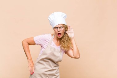 Orta yaşlı fırıncı kadın ciddi ve meraklı görünüyor, dinliyor, gizli bir konuşma veya dedikodu duymaya çalışıyor, kulak misafiri oluyor.