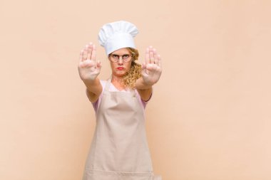 Orta yaşlı fırıncı kadın ciddi, mutsuz, kızgın ve hoşnutsuz görünüyor. Girmeyi yasaklıyor ya da her iki avuçta da dur diyor.