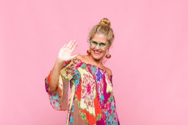 Orta yaşlı bir kadın mutlu ve neşeli bir şekilde gülümsüyor, el sallıyor, sizi selamlıyor ve selamlıyor, ya da veda ediyor.