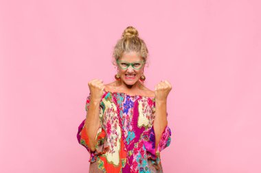 Orta yaşlı bir kadın sinirli bir ifadeyle ya da yumruklarıyla başarıyı kutlarken agresif bir şekilde bağırıyor.