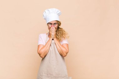 Orta yaşlı fırıncı mutlu, şanslı ve şaşkın görünüyor. İki eliyle ağzını kapatıyor.