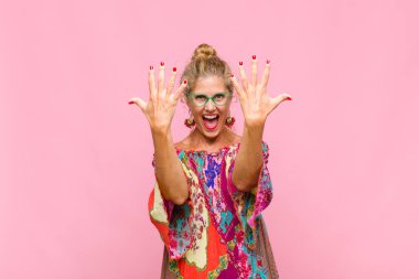 Orta yaşlı bir kadın gülümsüyor ve arkadaş canlısı görünüyor, onuncu veya onuncu numarayı gösteriyor, eli önde, geriye doğru sayıyor.