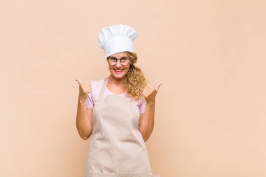 Orta yaşlı fırıncı neşeli gülümseyen ve mutlu görünen, kaygısız ve pozitif hisseden iki başparmağıyla