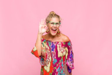 Orta yaşlı bir kadın kendini başarılı ve tatmin olmuş hissediyor ağzı açık gülümsüyor, elle işaret veriyor.