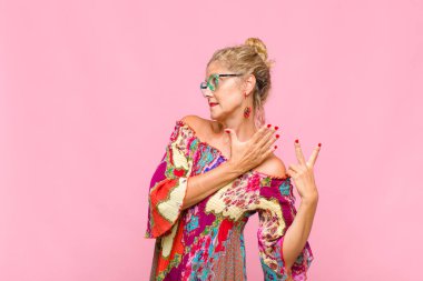 Orta yaşlı bir kadın gülümsüyor ve arkadaş canlısı görünüyor, 8 ya da 8 numarayı gösteriyor, elleri önde, geriye doğru sayıyor.