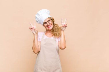 Orta yaşlı kadın fırıncı gülümsüyor ve mutlu görünüyor, arkadaş canlısı ve tatmin olmuş, zafer ya da barış işareti yapıyor.