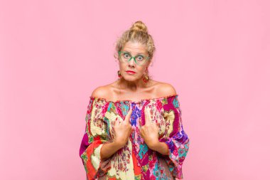 Orta yaşlı bir kadın, şaşkın ve tuhaf bakışlarıyla kendini işaret ediyor. Seçildiğine şaşırmış ve şaşırmış.