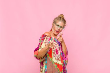 Olumlu, başarılı, mutlu bir tavırla gülümseyen orta yaşlı bir kadın kamerayı işaret ederek, elleriyle silah işareti yapıyor.