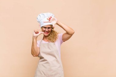 Orta yaşlı bir fırıncı mutlu, arkadaş canlısı ve pozitif hissediyor, gülümsüyor ve elleriyle bir portre veya fotoğraf çerçevesi yapıyor.