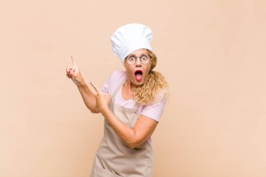 Orta yaşlı fırıncı kendini neşeli ve şaşırmış hissediyor. Şok olmuş bir ifadeyle gülümsüyor ve yan tarafı işaret ediyor.