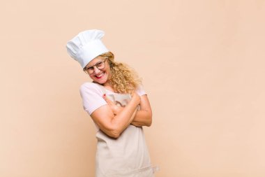 Orta yaşlı fırıncı kollarını kavuşturup mutlu bir şekilde gülüyor, rahat, pozitif ve tatmin edici bir pozla.