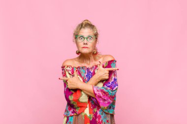 Orta yaşlı kadın şaşkın ve şaşkın görünüyor, güvensiz ve şüpheyle zıt yönleri işaret ediyor.