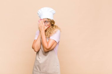 Orta yaşlı kadın fırıncı korkmuş ya da utanmış hissediyor, gözleri yarı kapalı ya da elleri kapalı gözetliyor ya da dikizliyor.