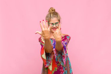 Orta yaşlı bir kadın gülümsüyor ve dost canlısı görünüyor, 7 ya da 7 numarayı gösteriyor, eli önde, geriye doğru sayıyor.