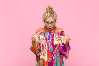 Orta yaşlı bir kadın şaşkın, ağzı açık ve şaşırmış, inançsızlık ve şaşkınlık içinde bakıyor ve onu işaret ediyor.