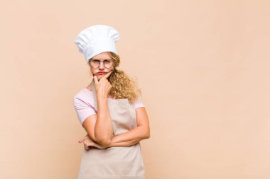 Orta yaşlı fırıncı kadın ciddi görünüyor, kafası karışık, kararsız ve düşünceli, seçenekler ve seçenekler arasında şüpheci.