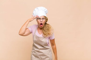 Orta yaşlı kadın fırıncı mutlu, şaşkın ve şaşırmış görünüyor, gülümsüyor ve inanılmaz ve inanılmaz iyi haberleri fark ediyor.