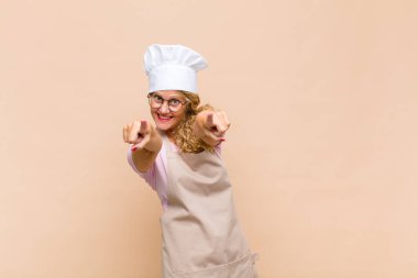 Orta yaşlı fırıncı kendini mutlu ve kendinden emin hissediyor, kamerayı iki eliyle gösteriyor ve gülüyor, seni seçiyor.