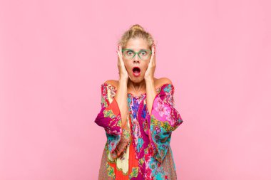 Orta yaşlı kadın mutsuz, korkmuş ya da endişeli görünüyor, ağzı sonuna kadar açık ve iki kulağını da elleriyle kapatıyor.