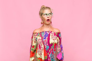 Orta yaşlı kadın şaşkın, mutlu, şaşkın ve şaşırmış hissediyor, ağzı açık bir şekilde yana bakıyor.