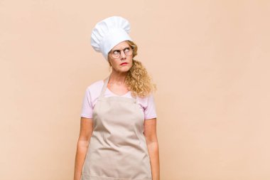 Orta yaşlı fırıncı kadın endişeli, kafası karışık, budala bir ifadeyle kopya alanı arıyor, şüpheci.