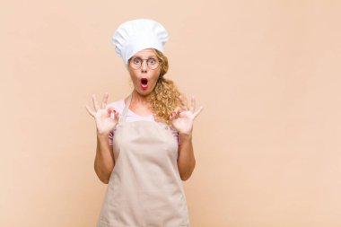 Orta yaşlı fırıncı şaşkın, şaşırmış ve şaşırmış hissediyor. Onaylıyor. İki eliyle işaret veriyor.