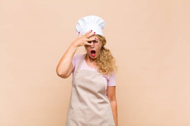 Orta yaşlı fırıncı kadın şok olmuş, korkmuş ya da korkmuş görünüyordu. Yüzü elle kaplıydı ve parmaklarının arasından bakıyordu.