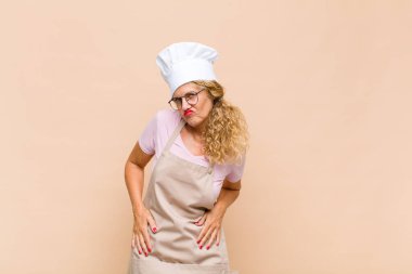 Orta yaşlı kadın fırıncı gururlu, kendinden emin, havalı, küstah ve küstah görünüyor, gülümsüyor, başarılı hissediyor.