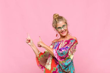 Orta yaşlı kadın mutlu bir şekilde gülümsüyor ve her iki elinde fotokopi uzayında nesne gösteriyor.