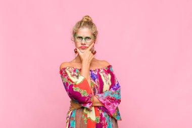 Orta yaşlı bir kadın ciddi, düşünceli ve güvensiz görünüyor, bir kolu çapraz ve çenesi üzerinde, seçenekleri tartıyor.