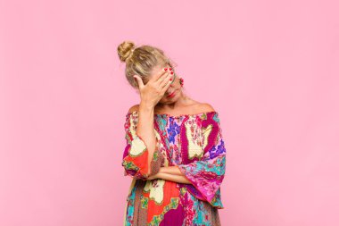 Orta yaşlı bir kadın stresli, utanmış ya da üzgün görünüyor, baş ağrısı var, yüzünü elle kapatıyor.