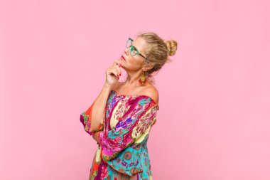 Orta yaşlı bir kadın düşünceli, meraklı ya da hayal kuruyor, hayal kuruyor ve uzayı kopyalamak için yukarı bakıyor.