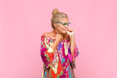 Orta yaşlı kadın boğazı ağrıyan ve grip belirtileri gösteren ağzı kapalı öksüren bir hasta.