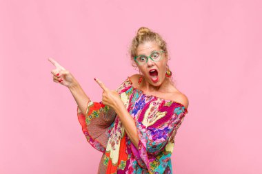 Orta yaşlı bir kadın mutlu ve şaşırmış hissediyor. Şok olmuş bir ifadeyle gülümsüyor ve bir tarafı işaret ediyor.